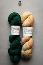 Load image into Gallery viewer, Two skeins of yarn, one green and one beige with green speckles, on a gray background.