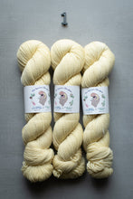 Load image into Gallery viewer, Three skeins of cream-colored yarn with labels on a gray background
