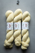 Load image into Gallery viewer, Three skeins of cream-colored yarn with labels on a gray background