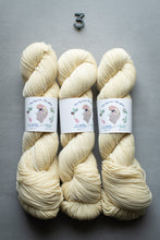 Load image into Gallery viewer, Three skeins of cream-colored yarn on a gray background with labels.