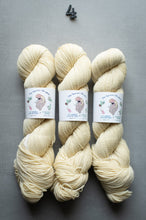Load image into Gallery viewer, Three skeins of cream-colored yarn with labels on a gray background