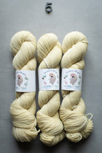 Load image into Gallery viewer, Three skeins of cream-colored yarn with labels on a gray background