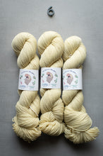 Load image into Gallery viewer, Three skeins of cream-colored yarn with labels on a gray background