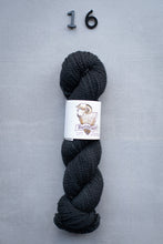 Load image into Gallery viewer, Dark gray skein of yarn with a label on a gray background