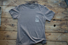 Load image into Gallery viewer, A gray short-sleeve crewneck t-shirt with a small white graphic print on the left chest, laid flat on a rustic wooden plank surface.