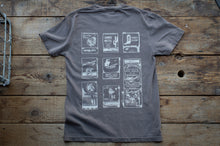 Load image into Gallery viewer, A dark gray t-shirt laid flat on a rustic wooden plank surface, showing the back side with a white graphic print of vintage album covers.