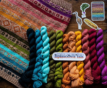 Load image into Gallery viewer, A knitted textile with multicolored horizontal stripes and a row of matching yarn skeins in dark blue, turquoise, olive green, mustard yellow, peach, pink, and magenta, arranged on a wooden surface. A white label reads 'lipissoowa tsis' over the center, with small decorative cutouts on the right.