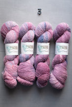 Load image into Gallery viewer, Four skeins of pink and purple yarn with labels on a gray surface.