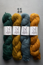 Load image into Gallery viewer, Four skeins of yarn in green, yellow, and blue on a gray background with a label.