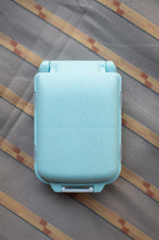 Load image into Gallery viewer, A light blue speckled hard plastic lunch box with a hinged lid, shown from a top-down view on a gray and beige striped fabric background.