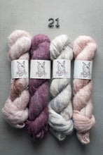 Load image into Gallery viewer, Four skeins of yarn in pink, purple, white, and pink with a label on a gray background.