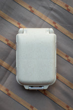 Load image into Gallery viewer, A light beige speckled hard-shell case, likely a compact cooler or travel case, shown from a top-down view on a striped fabric background.