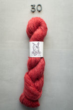 Load image into Gallery viewer, Red skein of yarn with a label on a gray background
