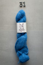 Load image into Gallery viewer, Blue skein of yarn with a label on a gray background