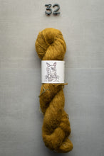 Load image into Gallery viewer, Mustard yellow yarn skein with a label on a gray background