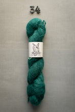Load image into Gallery viewer, Teal skein of yarn with a label on a gray background
