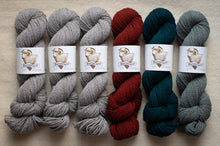 Load image into Gallery viewer, Six skeins of yarn in gray, red, and green on a beige surface with &#39;Bee &amp; Wolf&#39; labels.