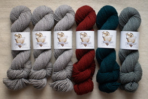 Six skeins of yarn in gray, red, and green on a beige surface with 'Bee & Wolf' labels.