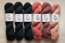 Load image into Gallery viewer, Three skeins of black yarn and three skeins of pink yarn with labels on a beige surface