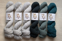 Load image into Gallery viewer, Six skeins of yarn in gray, black, and teal on a beige surface with brand labels.