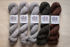 Five skeins of yarn in gray, black, and brown on a beige surface with 'Conte' labels.