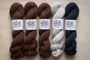Five skeins of yarn in brown, gray, and navy on a beige background with 'Couture Yarns' labels.