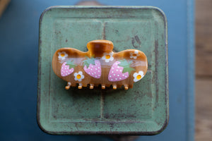 Decorative hair clip with strawberry design on a green metal surface