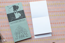 Load image into Gallery viewer, A folded art print or card set titled 'SISTERS UNITED' lies on a patterned pink and orange surface next to an open blank white card.