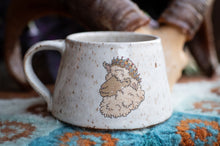Load image into Gallery viewer, White ceramic mug with a decorative sheep design on a textured surface