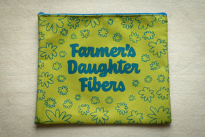 Yellow pouch with floral pattern and 'Farmer's Daughter Fibers' text on a beige surface