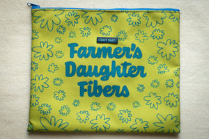 Yellow fabric pouch with floral patterns and 'Farmer's Daughter Fibers' text on a light wooden surface.