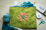 Green floral-patterned pouch with yarn and knitting tools on a beige surface