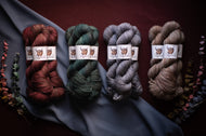 Four skeins of yarn in red, green, gray, and brown on a dark fabric background.