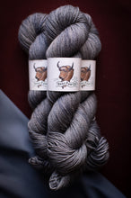 Load image into Gallery viewer, Three skeins of gray yarn with a brand label on a dark background