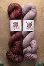 Load image into Gallery viewer, Two skeins of yarn, one red-brown and one pinkish-purple, with labels on a beige background.