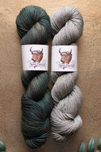 Load image into Gallery viewer, Two skeins of yarn, one green and one gray, with labels on a beige background.