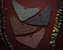 Load image into Gallery viewer, Four triangular knitted coasters in different colors on a dark brown background with leafy edges.