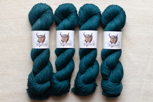Four skeins of teal yarn with labels on a beige background
