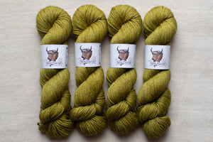 Four skeins of green yarn with labels on a beige background