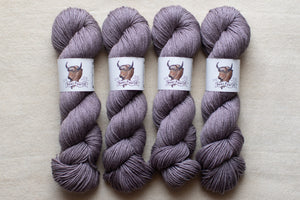 Four skeins of purple yarn with labels on a beige background