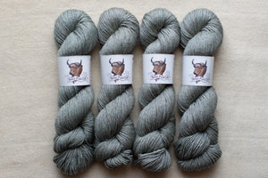 Four skeins of gray yarn with labels on a beige background