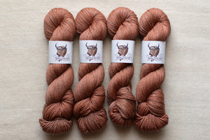 Four skeins of brown yarn with labels on a beige background