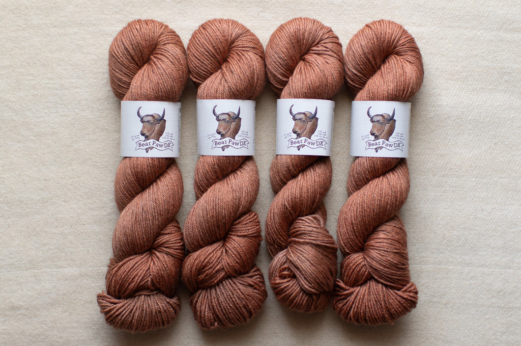 Four skeins of brown yarn with labels on a beige background