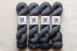 Four skeins of gray yarn with labels on a beige background