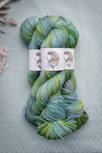 Load image into Gallery viewer, Multicolored skein of yarn with a label on a textured surface