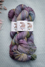 Load image into Gallery viewer, Multicolored skein of yarn with a label on a textured gray background