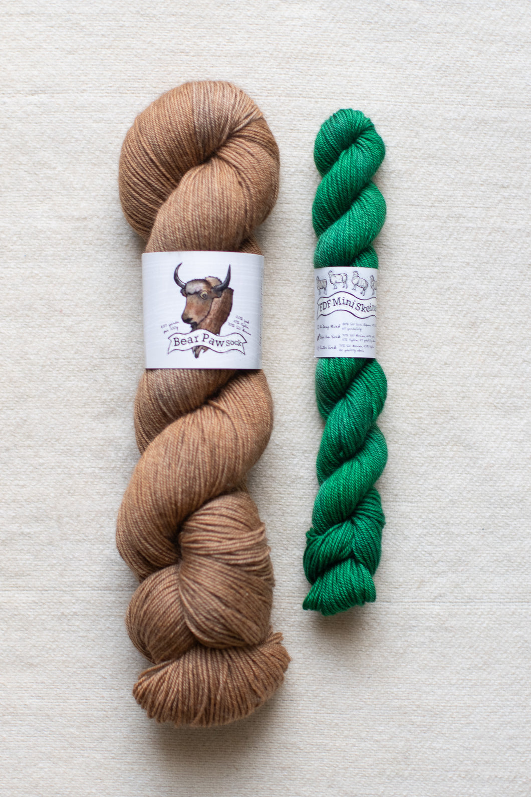 Two skeins of yarn, one brown and one green, on a light background.
