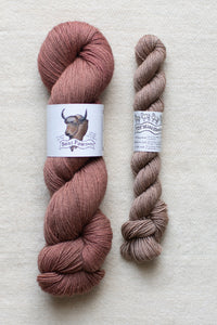 Two skeins of yarn, one pink and one brown, on a textured surface with labels.