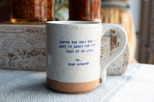 Load image into Gallery viewer, A speckled ceramic mug with a brown base and blue printed text reading 'YOU'RE THE ONLY ONE I WANT TO ANNOY FOR THE REST OF MY LIFE. XO, YOUR HUSBAND', set on a textured light blue surface with a blurred rustic background.