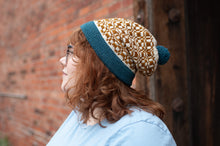 Load image into Gallery viewer, Person wearing a patterned beanie with a blue band against a brick wall.